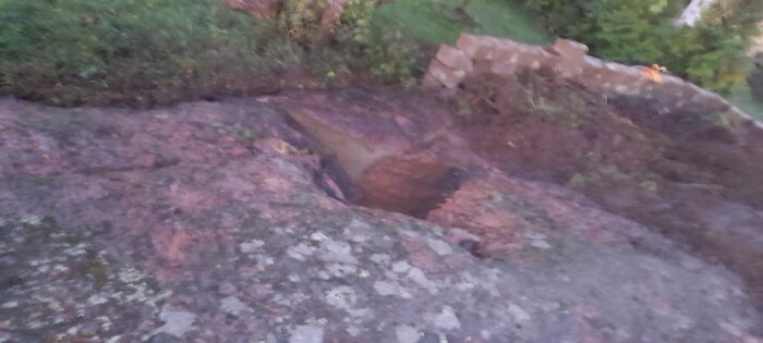 Bergslänt med ett litet hål i trädgården, omgiven av stenar och grönska, potentiell plats för en mini-damm.