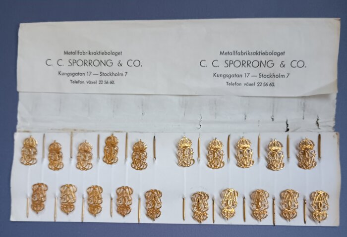 Guldfärgade emblem med kronor från C. C. Sporrong & Co på en kartong.