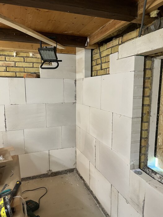 Renovering av korsvirkeslänga med synlig lättbetong- och tegelvägg, takbjälkar och byggutrustning i ett halvfärdigt rum.