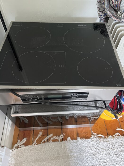 Induktionshäll med fyra plattor i ett kök, ovanpå en inbyggnadsugn, med en reflekterande yta av rostfritt stål.