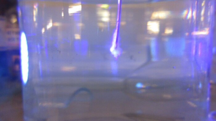 En suddig vy av en ljusbrytning genom en genomskinlig cylinder med ett ljusblått sken i bakgrunden, tagen i ett laboratorium.