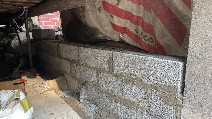 Murad och armerad vägg med verktyg och material, inklusive en sprayflaska och byggplast, i ett pågående byggprojekt.