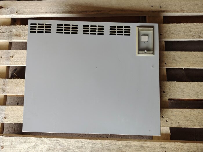 Gammalt elelement från 70- eller 80-talet liggandes på en träpall, med del av en strömbrytarpanel synlig på högra sidan.