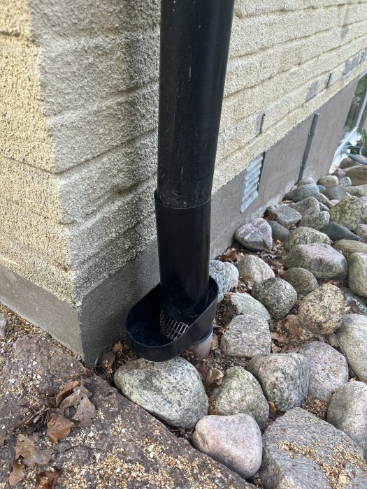 Stuprör vid en husgrund med dräneringsrör och stenar, problem med fukt.