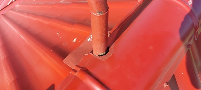 Rött tak med ett rör som står upp. Plåten kring mynningen verkar inte tätt, skapar en glipa vid avloppsluftningen. Nockplåt klippt fel.