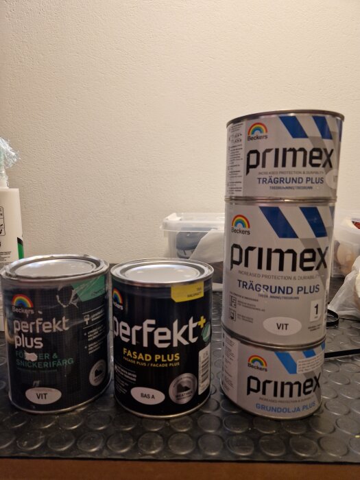 Fyra färgburkar från Beckers, inklusive "Perfekt Plus Fönster & Snickerifärg", "Perfekt Fasad Plus", "Primex Trägrund Plus", och "Primex Grundolja Plus".