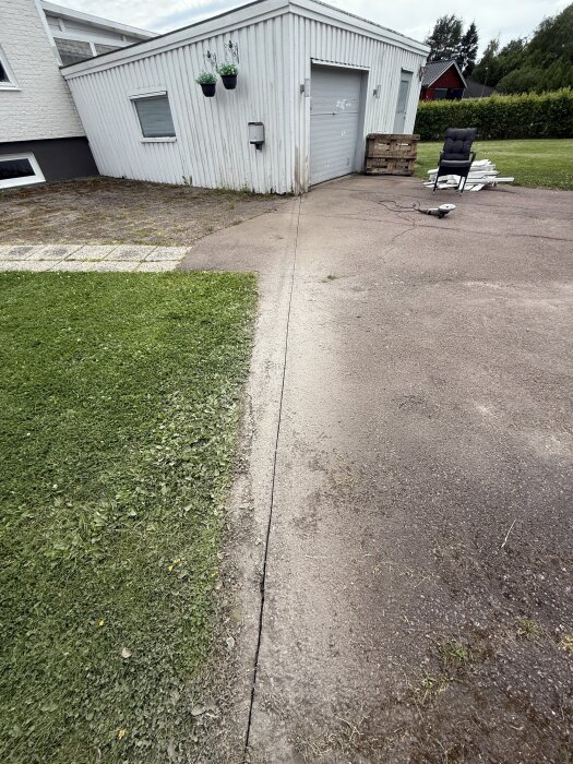 Rak linje kapad i asfalt utanför garage för att skapa avgränsning mot gräs, med stol och material staplat bredvid.