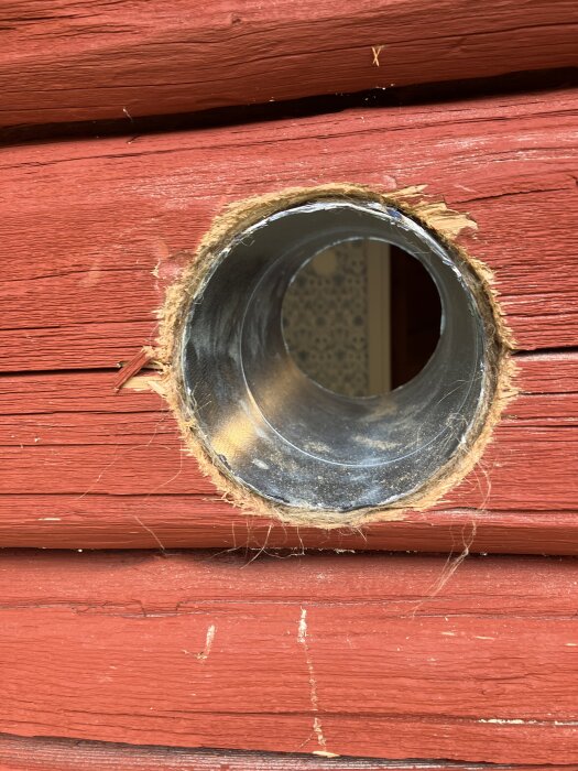 Hål borrat i röd trävägg med en pro-fit 105mm såg, visar trät och metallkant inuti hålet.