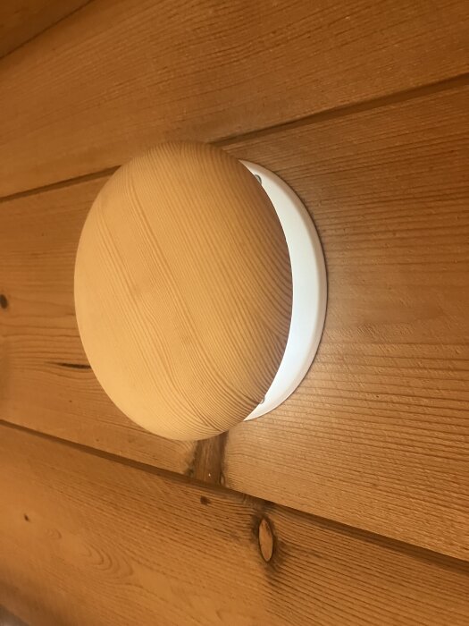 Träpanelvägg med rund öppning som visar ett inbyggt rör eller en lampa i ett sommarhus, troligen gjort med pro-fit 105mm verktyg.