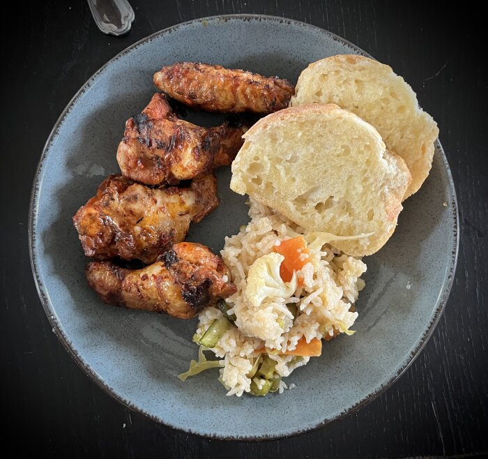 Grillade chicken wings, vitlöksbröd och ris med grönsaker på tallrik.