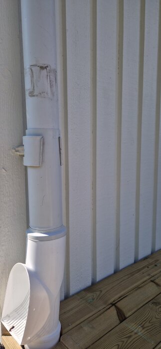 Stuprör med monterad renstratt och brunnsutkastare, klämma sitter löst och rören sluter inte tätt, intill vägg och trätrall.