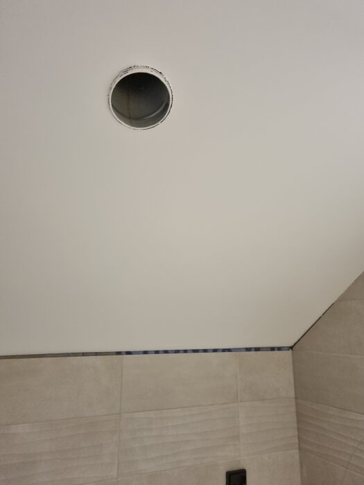 Ventilationsrör i taket på ett badrum, avslutat med en 125mm spiro-böj, i nivå med ytan av målad gips.