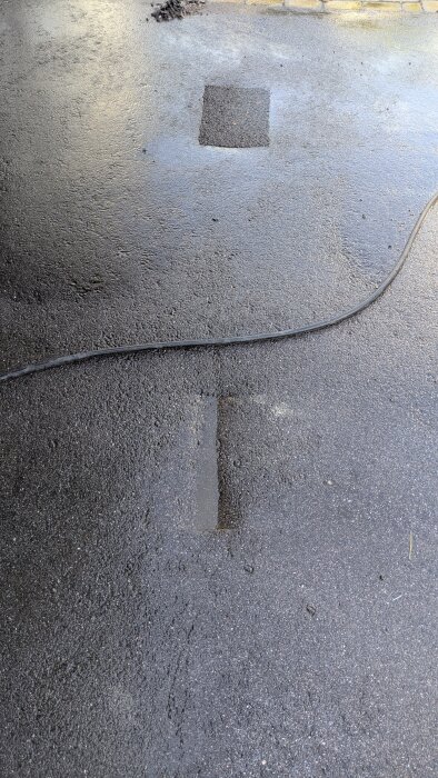 Uppsågat och lagat asfaltshål på byggarbetsplats, med skarv synlig bredvid en kabel på marken.