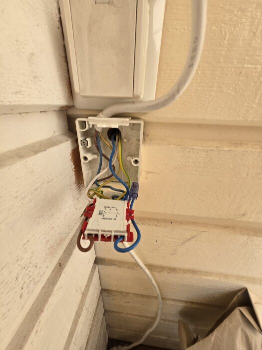 Bortmonterad strömbrytare med exponerade elkablar monterad på en vit träväggsfasad.