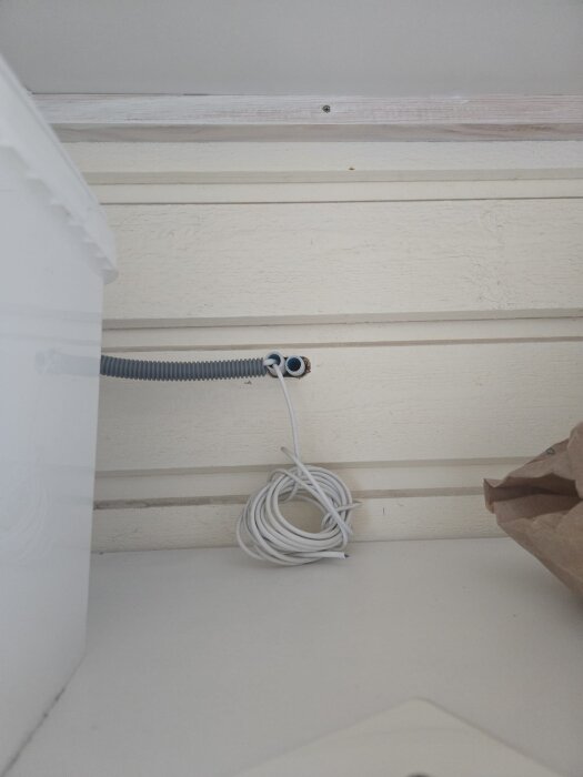 Kabel med kopparledare syns i änden av ett flexrör mot en trävägg, med en rulle kabel liggande bredvid.