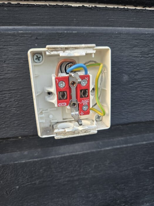 En öppen elektrisk brytare med exponerade kablar monterad på en svart vägg. Kablarnas placering diskuteras i inlägget.