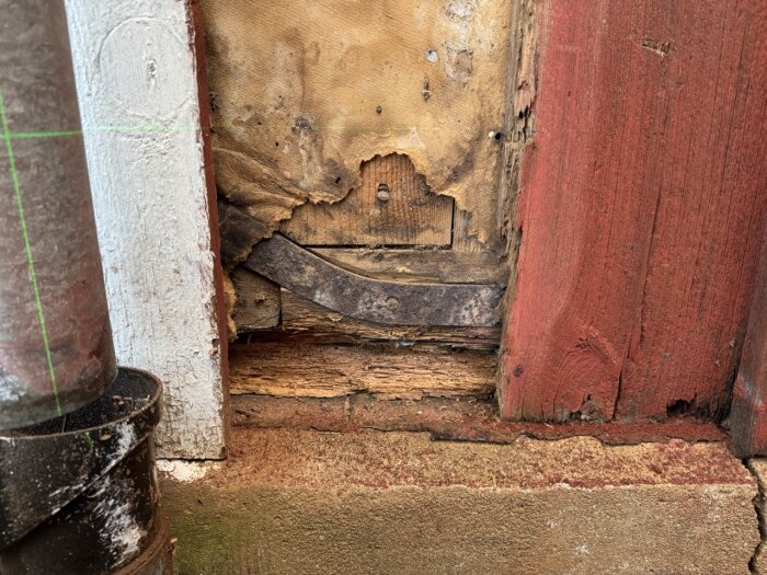 Skadad väggpanel nära ett stuprör med sliten träbalk och laserlinje på fasad, visar potentiell fuktskada på ett gammalt hus.