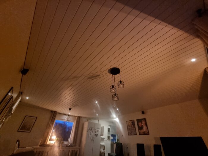 Modernt inrett rum med vit träpanel i taket, hängande lampa, stora fönster med gardiner, och dekorerade väggar med tavlor.