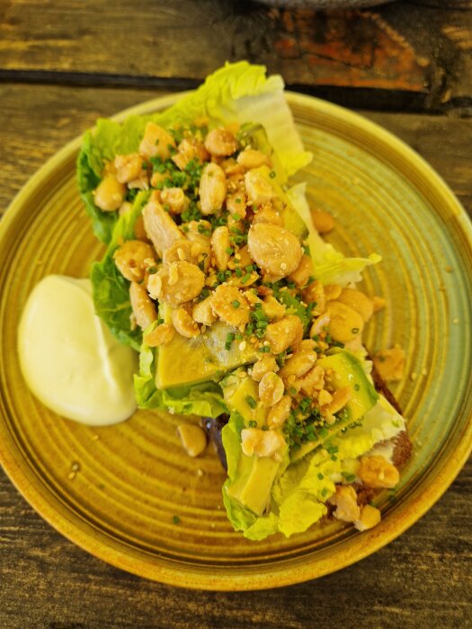 Avokado på gemsallad med kavring och Marconamandlar, serverad på en tallrik med en klick sås, fotograferad utomhus på en träyta.