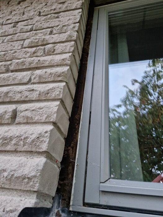 Fönster monterad mot tegelvägg med borttaget foder, visar hörn och kantdetaljer av byggprojekt.