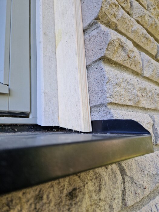 Fönsterkarm av trä monterad på tegelvägg, med svart fönsterbleck. Arbete med nykapat trä redo för att oljas och målas.