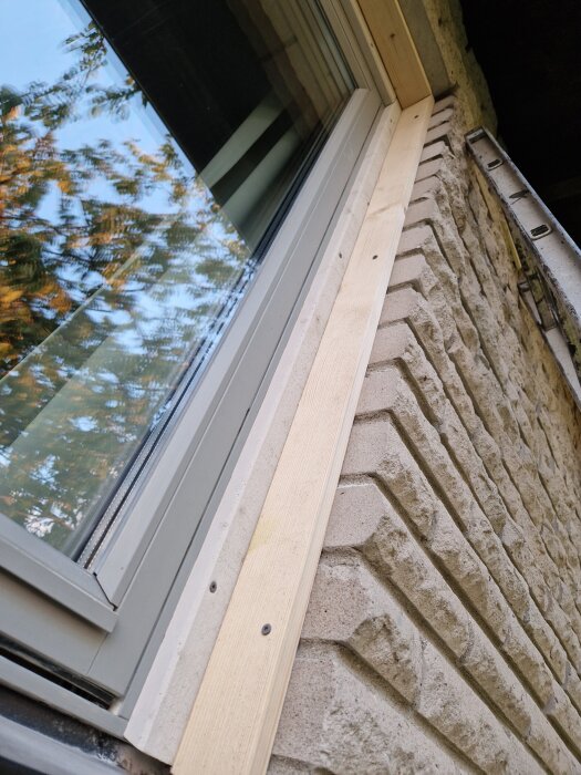 Fönster med nyligen monterad träram på stenfasad, skruvar synliga.