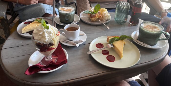 Fat med kaffe, kakor, bakverk och glass serverat på ett cafébord.