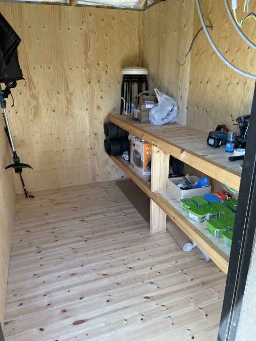 Förråd med arbetsbänk fylld med verktyg, förpackningar och stolar, nymålade träväggar och golv.