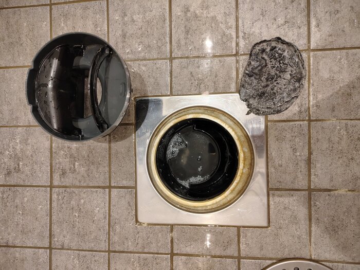 Avlägsnat vattenlås, golvbrunn och misstänkt gummiartat föremål på klinkergolv.