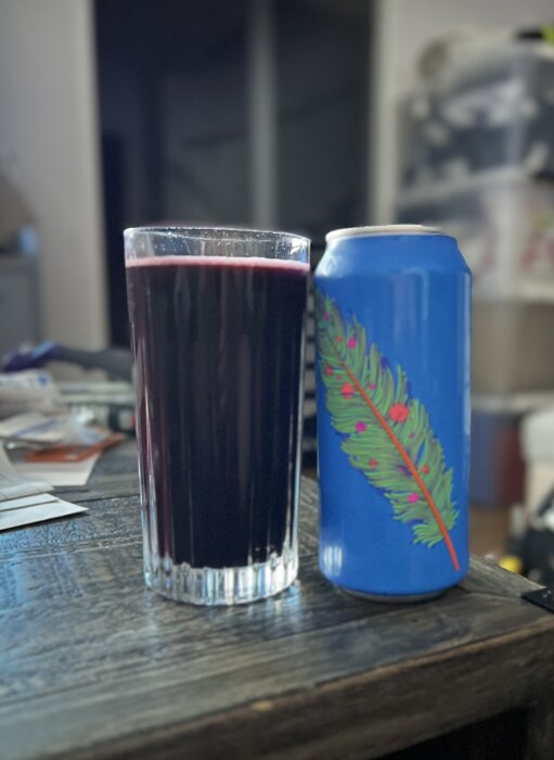 Glas med mörkröd dryck och en blå burk med fjädermotiv på ett bord.