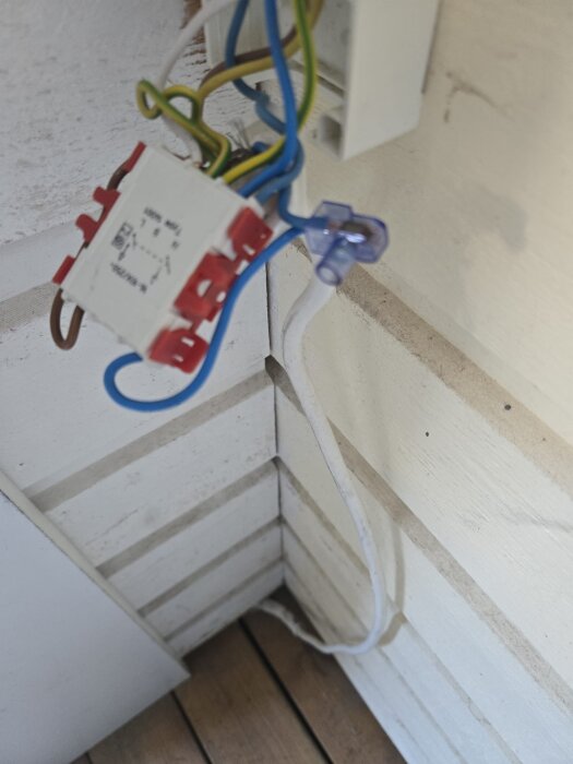 Elektriska kablar och kopplingsbox med exponerade ledningar på en veranda, en del av elinstallationen är synlig mot väggen.