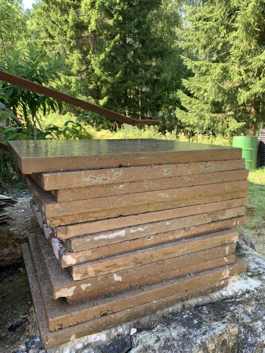 Fuktiga bruna stenplattor staplade utomhus, med en skog i bakgrunden.
