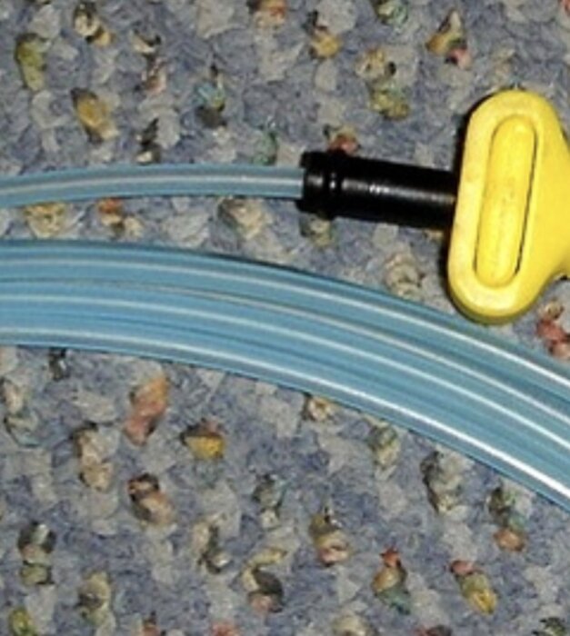 Plastslang med gul koppling på ett mönstrat golv, troligen en använd NONEL-slang för sprängningar, ofarlig och redan skjuten.