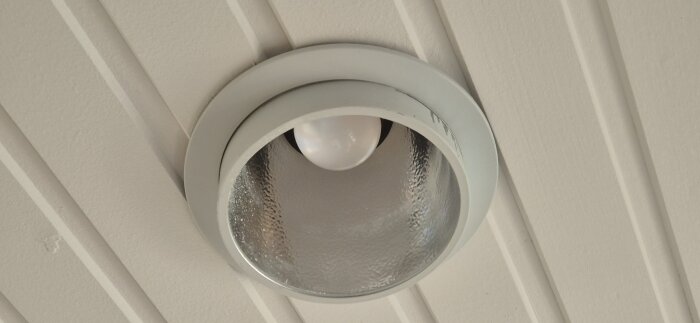 Infälld downlight i vitt tak från 70-talet, 150 mm diameter, E27-sockel, med synlig glödlampa och silverreflektor.
