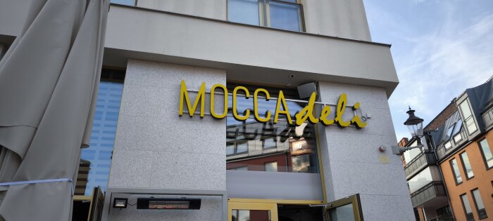 Ingång till kaféet Mocca deli med gul skylt på en modern byggnad i stadsområde.