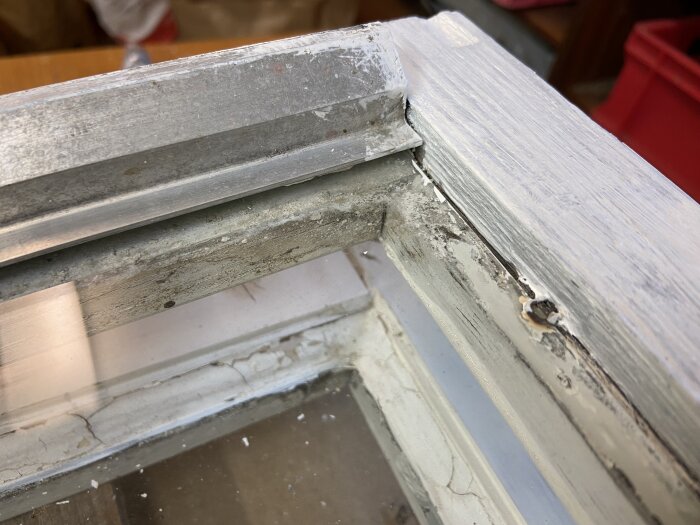 Gammalt 2-glas-fönster med vitmålad träram och metallfals i nederkant. Färgen flagnar, och kitt saknas mellan glaset och metallisten.