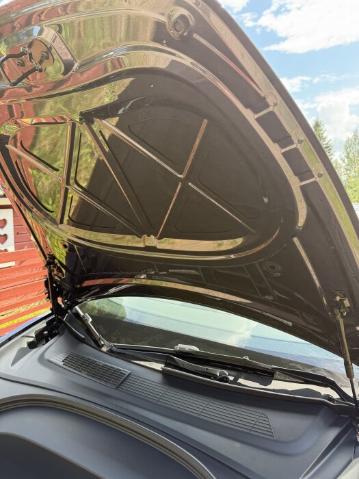 Bilens öppna frunk i dagsljus, med tydlig vy av motorhuvens insida och omgivning.
