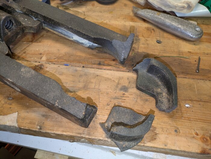 Trasig bladspänningsdel från en bandsåg på en arbetsbänk i trä, med metallverktyg i bakgrunden.