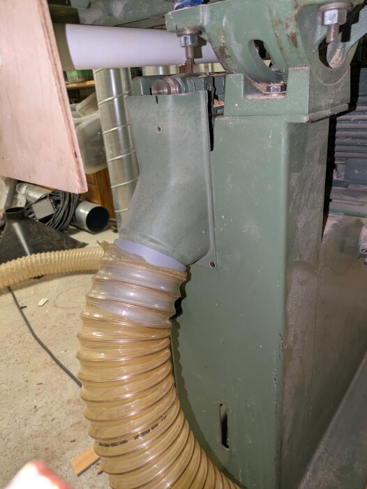 Grön bandsåg med trasig bladspänning och dammsugaranslutning i en verkstad. Visar maskindelarnas monteringsdetaljer.