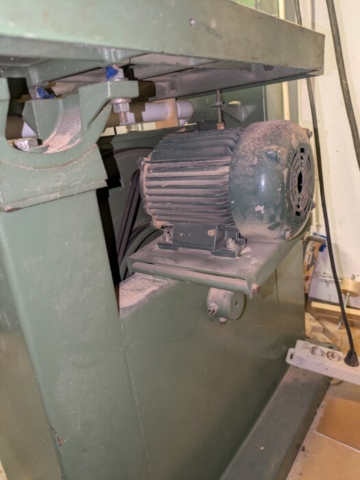 Bandsågsmotor och dess upphängning med damm på ytan, en del av sågens mekaniska struktur syns.