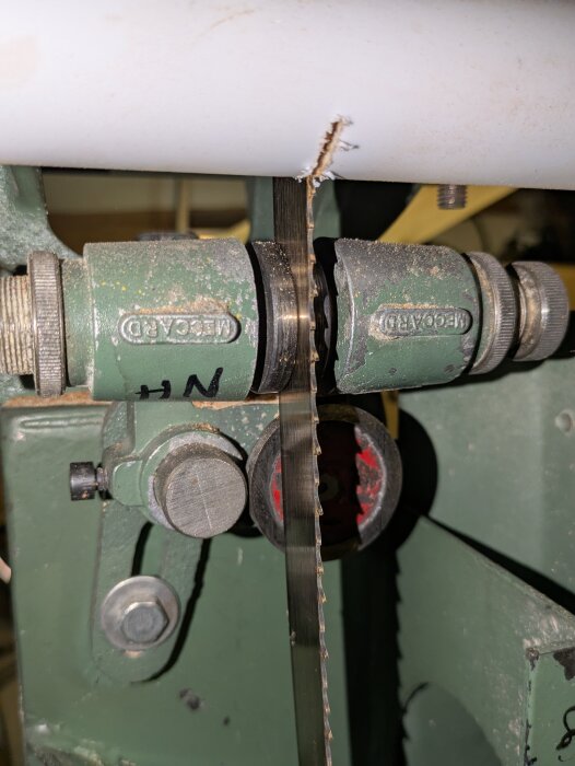 Närbild på en bandsåg med ett synligt sågblad och delar av spänningsmekanismen, märkning "MEGA" på sågens justeringar.