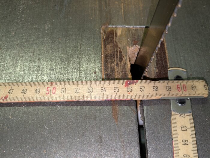 Närbild av en bandsåg med löst mätband över sågbordet, visar detaljer kring skärspåret och mätmått.