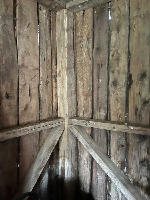 Gammal vedbod med träpanelväggar och förstärkningar i hörnet, inomhus.