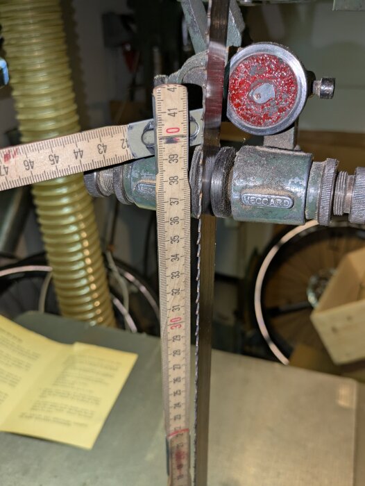 Närbild av en bandsåg där en måttstock är fastsatt nära bladet, omgiven av en verkstadsmiljö med några cykelhjul i bakgrunden.