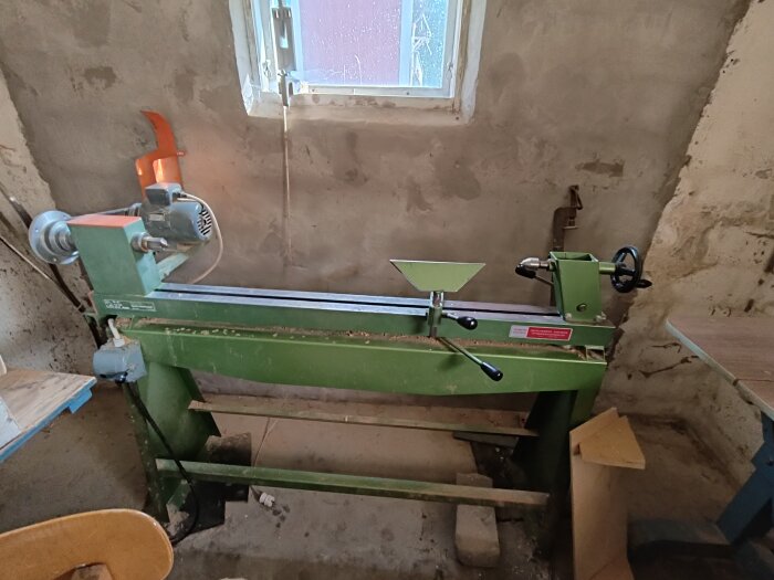 Grön svarv från 50-talet med stålstativ och kilremsdrift, placerad nära ett fönster i ett verkstadsutrymme.