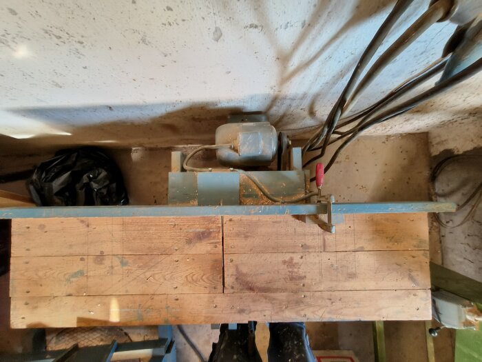 Träarbetsbänk med monterad maskin och synliga kablar, fotograferad uppifrån i en verkstadsmiljö.