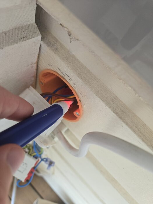 En person använder en penna för att undersöka en orange kopplingsdosa med elektriska ledningar.