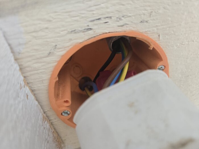 Närbild av en orange eldosa med flera kablar anslutna, monterad på en vit vägg.