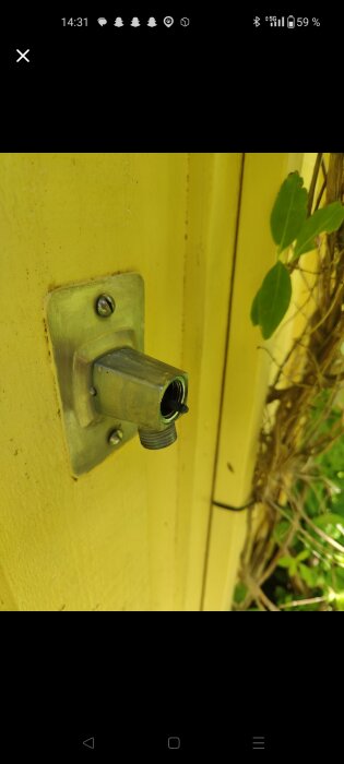 Äldre vattenutkastare från FM Mattsson monterad på en gul vägg, saknar kranöverdel.