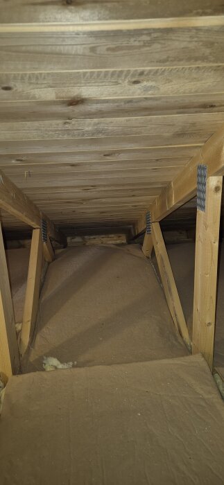 Vindsutrymme med trästruktur och isoleringsmaterial, potentiellt svartmögel synligt på taket.